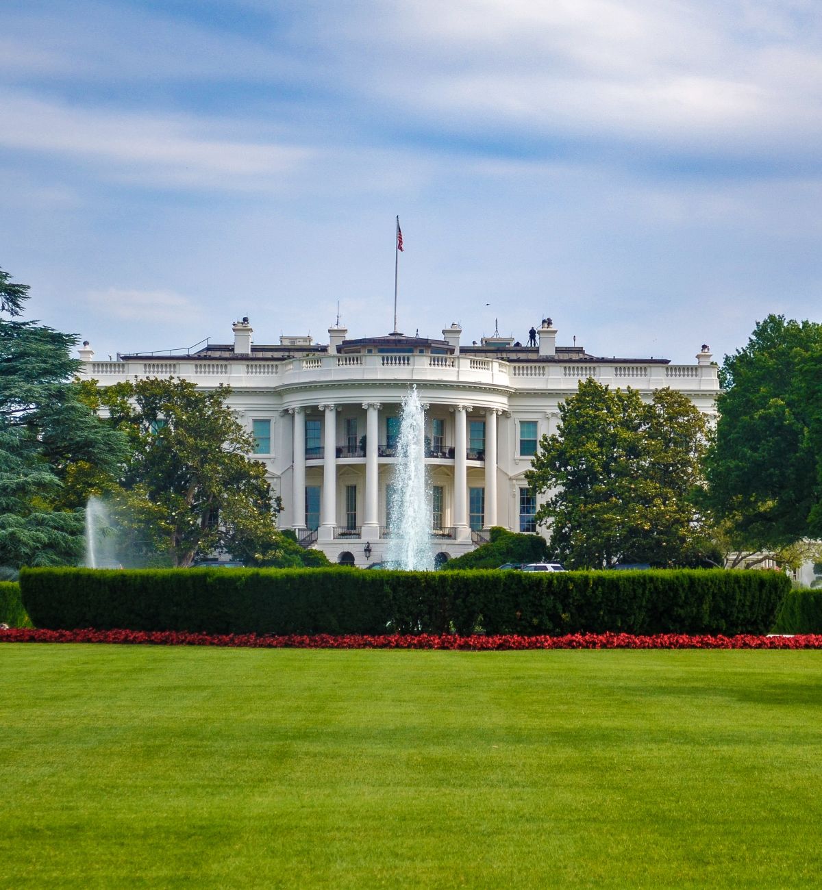 A Large Green Field With Trees In The Background With White House In The Background